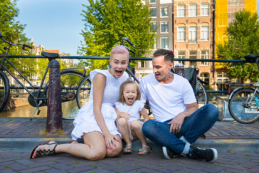 Familie fotosessie Amsterdam, On-location family photoshoot in Amsterdam, children Photoshoot, together with the family for a fun photo session, a happy little girl is having fun, sitting together with her parents, on a bridge over Brouwersgracht, Amsterdam