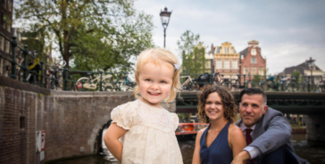 On-location family photoshoot in Amsterdam, children Photoshoot, together with the family for a fun photo session, a happy little girl is standing proud in front of the camera with her proud parents in the background, Brouwersgracht, Amsterdam