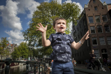 Familie fotosessie Amsterdam, On-location family photoshoot in Amsterdam, children Photoshoot, Family portrait, family photographer Amsterdam, portrait of a happy little boy jumping with a typical Amsterdam background, Amsterdam old city centre