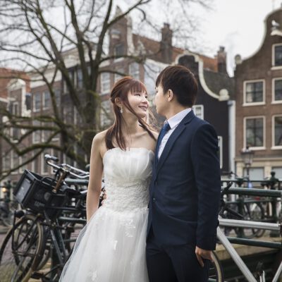 Couple photoshoot, engagement, elopement photoshoot, Asian bride and groom just eloped, posing in front of typical old houses by a canal in Amsterdam old city centre