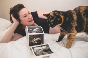 Maternity photographer, Pregnancy photography, lifestyle photoshoot, family photoshoot, photo of a woman pregnant chilling on her bed with focus on her baby twins' echograph photos and her cat looking at them, Amsterdam