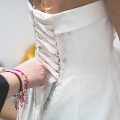 Wedding photography, marriage photographer, Bruidsfotograaf en trouwfotograaf, Zoom on the bridesmaid hand tightening up the bride’s dress corset, Amsterdam