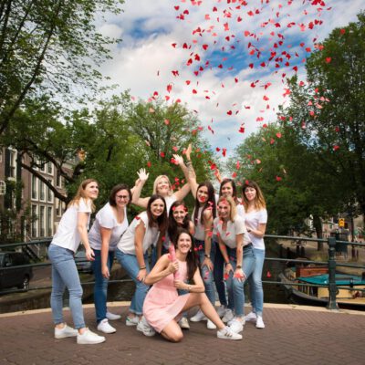 Bachelorette party photography EVJF, happy group of friends cheering and throwing red heart confetti's on a bridge over Reguliersgracht, Amsterdam