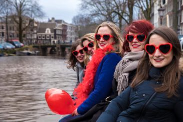 Bachelorette party photography EVJF, friends wearing red heart-shape sunglasses, sitting on a pontoon, near a romantic canal, having a good time, celebrating the bride-to-be, Brouwersgracht, Amsterdam