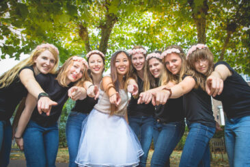 Bachelorette party photography EVJF, a group of ladies friends posing around the bride-to-be, having a good time and pointing their fingers to the camera, Hermitage Museum gardens, Amsterdam