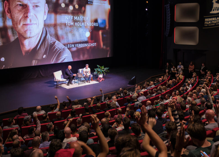 Event photography, festival photography, general view of a theatre room with audience and stage with Tom Holkenborg presenting a masterclass and answering question from the audience at NFF (Nederlands Film Festival) Utrecht