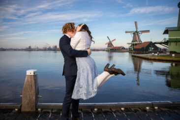 Engagement and proposal photography, couple photoshoot, portrait of a young couple in love just after the man proposed his girlfriend, she jumps in his arms, with a romantic winter landscape and the windmill of Zaanse Schans, The Netherlands