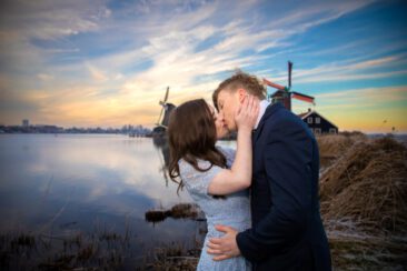 Engagement and proposal photography, couple photoshoot, portrait of a young couple in love kissing each other with love, with a romantic winter landscape and the windmill of Zaanse Schans, The Netherlands