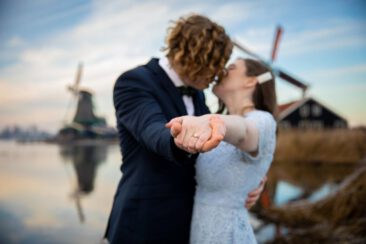Engagement and proposal photography, couple photoshoot, portrait of a young couple in love kissing with a zoom on the engagement ring, with romantic winter landscape and the windmill of Zaanse Schans, The Netherlands