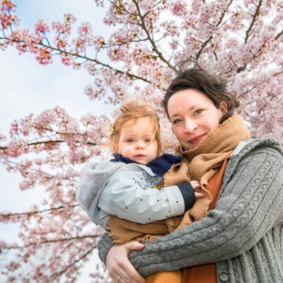 Family photoshoot, a mum is holding her little girl with blooming cherry tree in the background, Westerpark Amsterdam