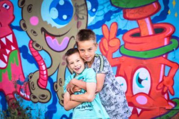Family and children Photoshoot in Amsterdam, together with the family for a fun photo session, Portrait photography, 2 happy young boys brothers hugging each other, in front of colorful graffitis, NDSM Amsterdam