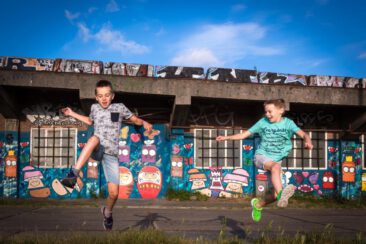 On-location family photoshoot in Amsterdam, children Photoshoot, together with the family for a fun photo session, 2 happy little boys are running and jumping on a sunny summer day in front of a wall with graffiti, NDSM, Amsterdam