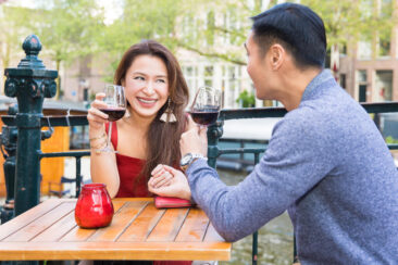 Couple photoshoot, loveshoot, engagement photoshoot: portrait of a couple sitting at a café terrace, having a glass of wine, looking at each other with love and complicity after proposal near romantic canal Prinsengracht, Amsterdam