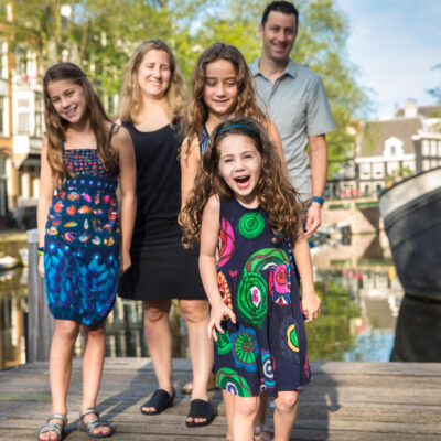 Familie fotosessie Amsterdam, On-location family photoshoot in Amsterdam, children Photoshoot, Family portrait, family photographer Amsterdam, Family photoshoot, a young girl is proudly standing with her proud parents and sisters in the background, on a pontoon by Brouwersgracht Canal in Amsterdam