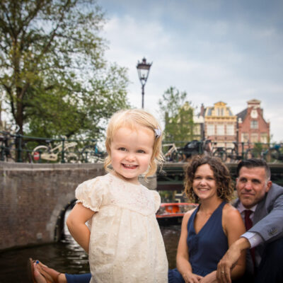 Familie fotosessie Amsterdam, On-location family photoshoot in Amsterdam, children Photoshoot, Family portrait, family photographer Amsterdam, a little girl is proudly standing with her proud parents in the background, on a pontoon by Brouwersgracht Canal in Amsterdam