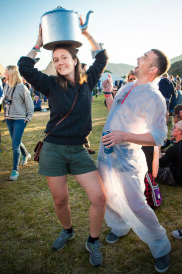 Event photography, festival photography, 2 festival visitors are having fun, a lady is carrying a giant kettle on her head and her boyfriend is laughing, Traena Festival, Norway