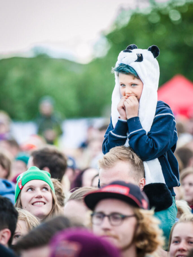 Event photography, festival photography, a young boy on his father shoulder in the audience crowd is watching a concert at Traena Festival, Norway