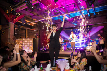 Corporate event photographer, Corporate party photography, singer up on a chair with colleagues celebrating in front of a live concert during Manulife gala dinner party at Harbour Club, Amsterdam