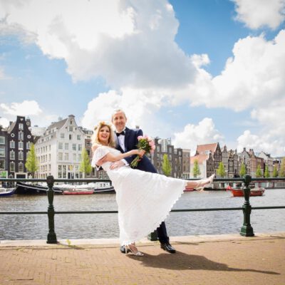 Elopement and wedding photography, happy bride and groom posing in front of the Amstel river by the Amsterdam city hall