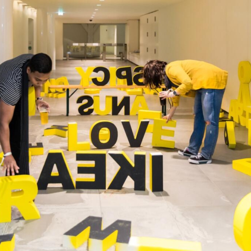 Cultural event photography, 2 young people are playing around with art installation big yellow letter at Museumnacht at Outsider Art Museum (Museum van de Geest in Hermitage Amsterdam