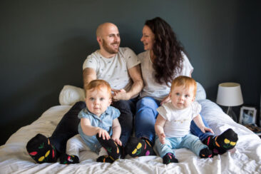 Baby photography, lifestyle photoshoot, family photoshoot, happy family posing on the parent's bed, mother, father and their 2 little twin baby girls, they are wearing assorted socks, Amsterdam