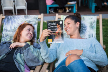 Event photography, festival photography, 2 ladies laying on a long chair are looking at the festival program, at open-air screening at WCA 2018 (World Cinema Amsterdam Festival) Marie Heinekeinplein Amsterdam
