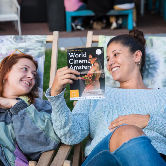 Event photography, festival photography, 2 ladies laying on a long chair are looking at the festival program, at open-air screening at WCA 2018 (World Cinema Amsterdam Festival) Marie Heinekeinplein Amsterdam
