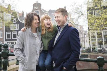 On-location family photoshoot in Amsterdam, children Photoshoot, together with the family for a fun photo session, a happy little girl is sitting on a bridge's rail in between her parents, Brouwersgracht, Amsterdam