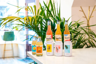 Food and restaurant photography, on-location branding and product photography, cans of lemonade, juice, and kombucha bottles presented on the bar in front of a plant