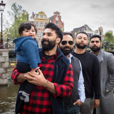Family photography, travel photographer, portrait of 4 men with a smiling happy baby boy are posing by Brouwersgracht canal in Amsterdam