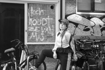 solo portrait photoshoot, lifestyle photography, black and white portrait of a young woman posing near bikes in a small street in Amsterdam city centre