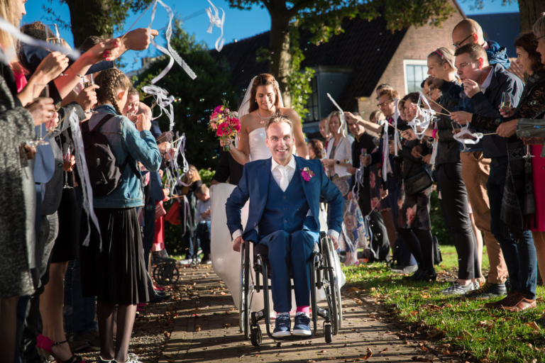 Wedding photography, elopement, a groom in a wheelchair and a bride are getting out the church ceremony surounded by their guests blowing bubble, Ouderkerke aan de Amstel