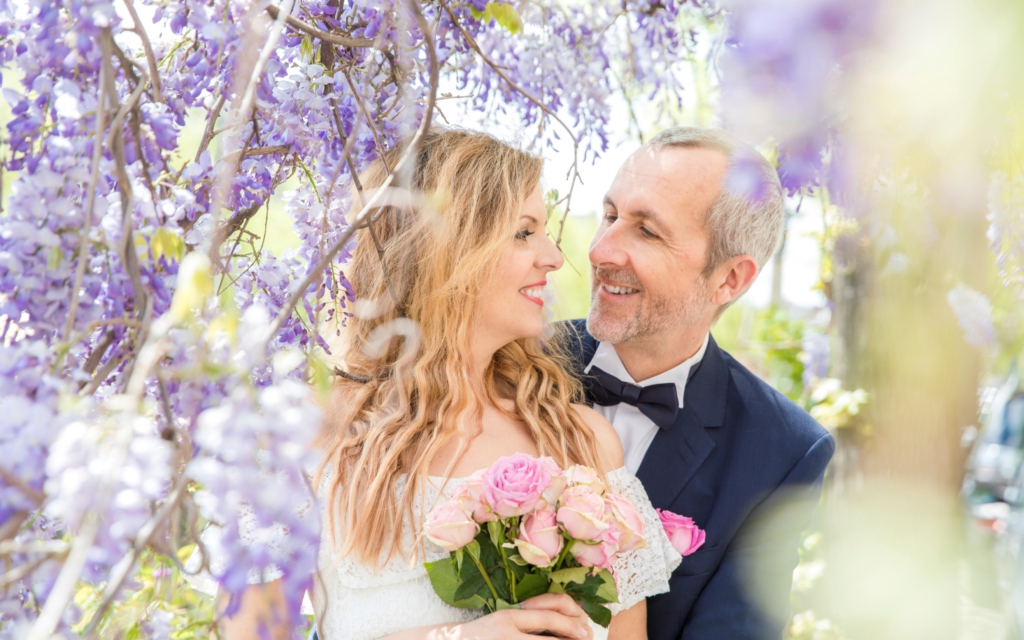 Wedding photography, elopement photographer, a groom and a bride are tenderly looking at each other under a wisteria in Amsterdam